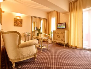 Ein Hotelzimmer mit großem Sessel, kleinem Tisch mit Topfpflanze, Fernseher auf einer Kommode und Spiegel an der Wand.