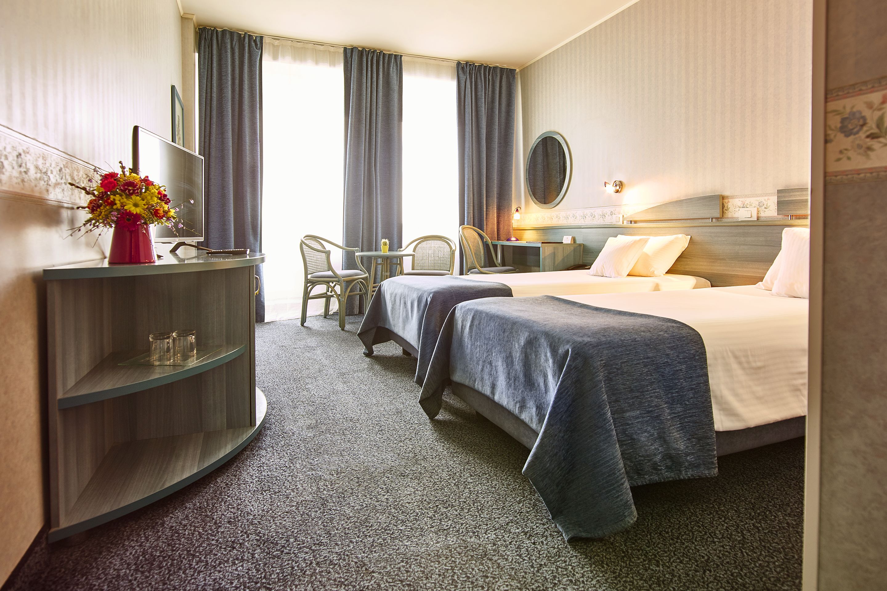 Habitación de hotel con cama, escritorio, silla, televisor y un florero.