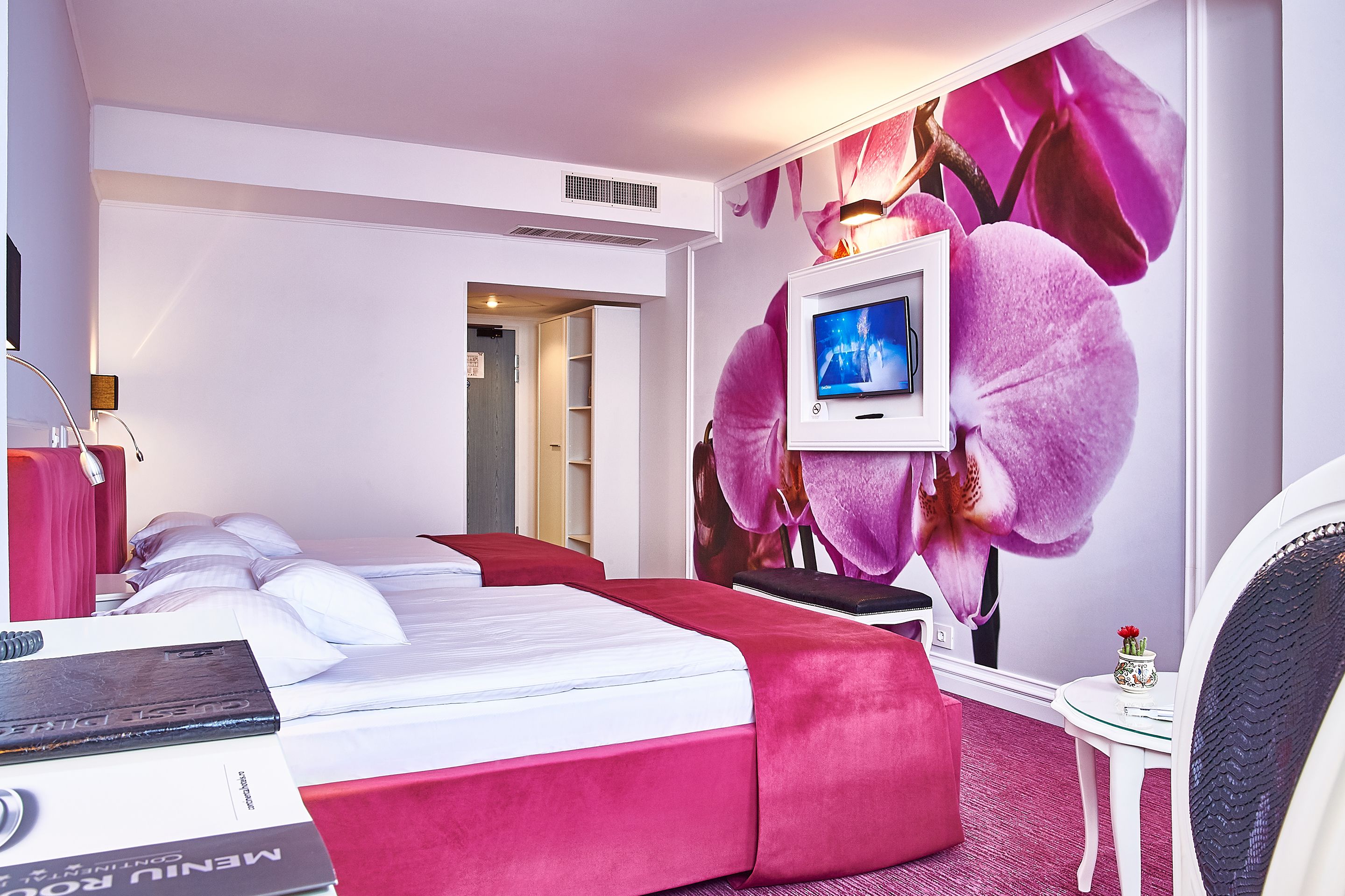 A hotel room with a bed, a TV, a small table, and a wall with a large flower mural.