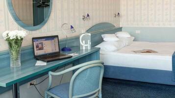 A hotel room with a bed, a desk with a laptop, a chair, a mirror, and a bedside table.