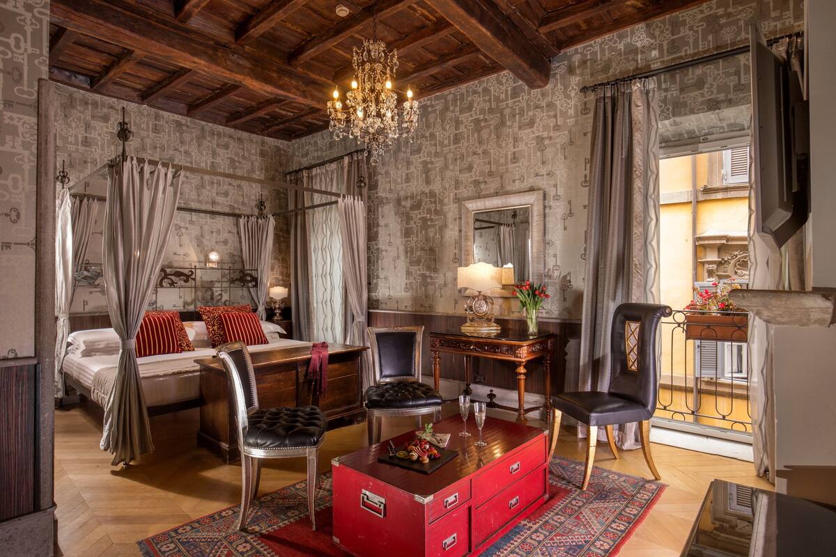 Une pièce comprenant un lit, une commode rouge, un lustre et un grand miroir.