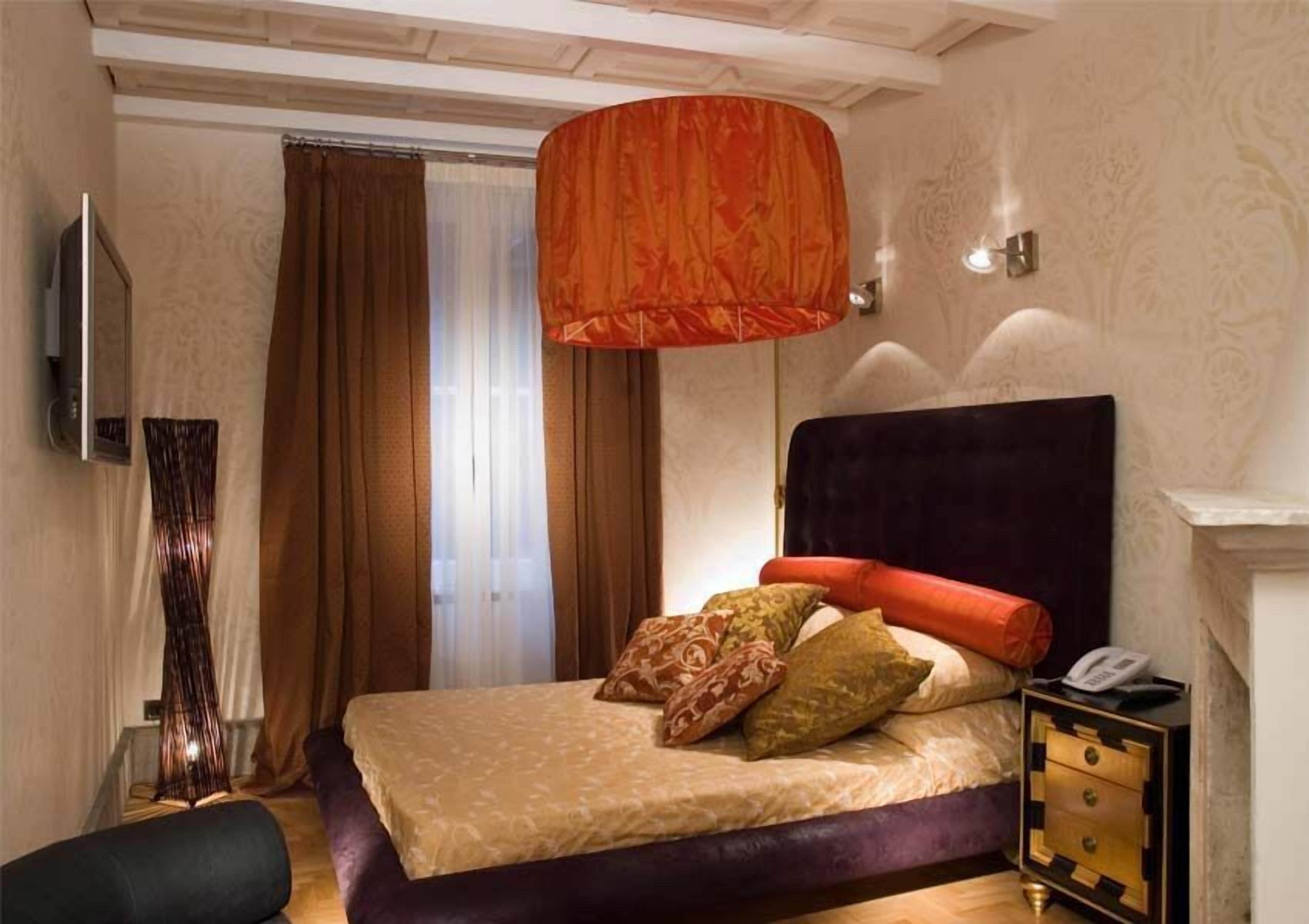A bedroom with a large bed, a nightstand, a lamp, and a wall-mounted TV.
