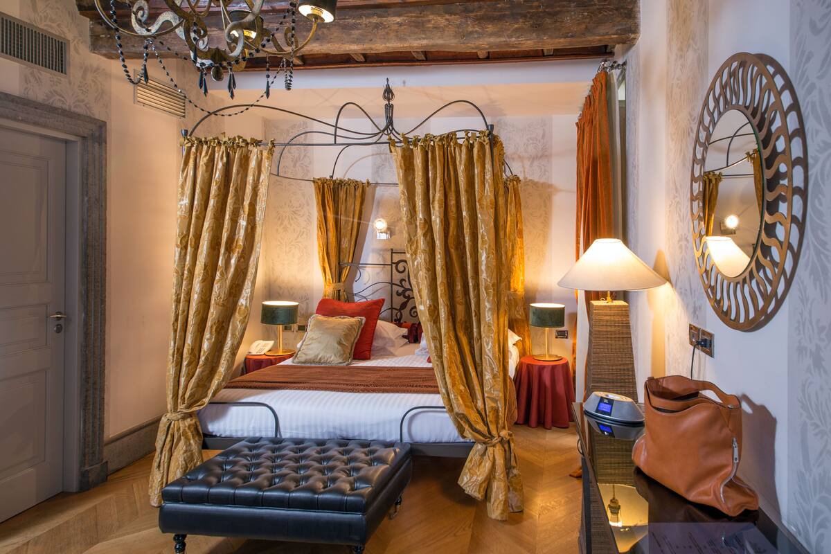 Une chambre à coucher avec un lit à baldaquin, deux tables de chevet, un banc et un miroir au mur.