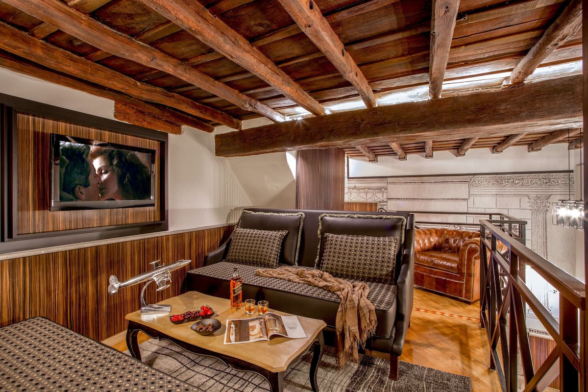 Un salon chaleureux avec un plafond en bois, un canapé en cuir, une table basse avec des magazines et une bouteille, et un téléviseur fixé au mur.