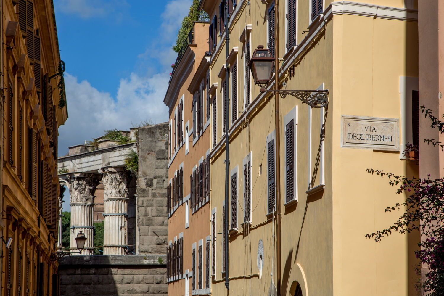 A narrow street with historic buildings, a stone archway, and a sign reading "VIA DEGL'IBERNESI".