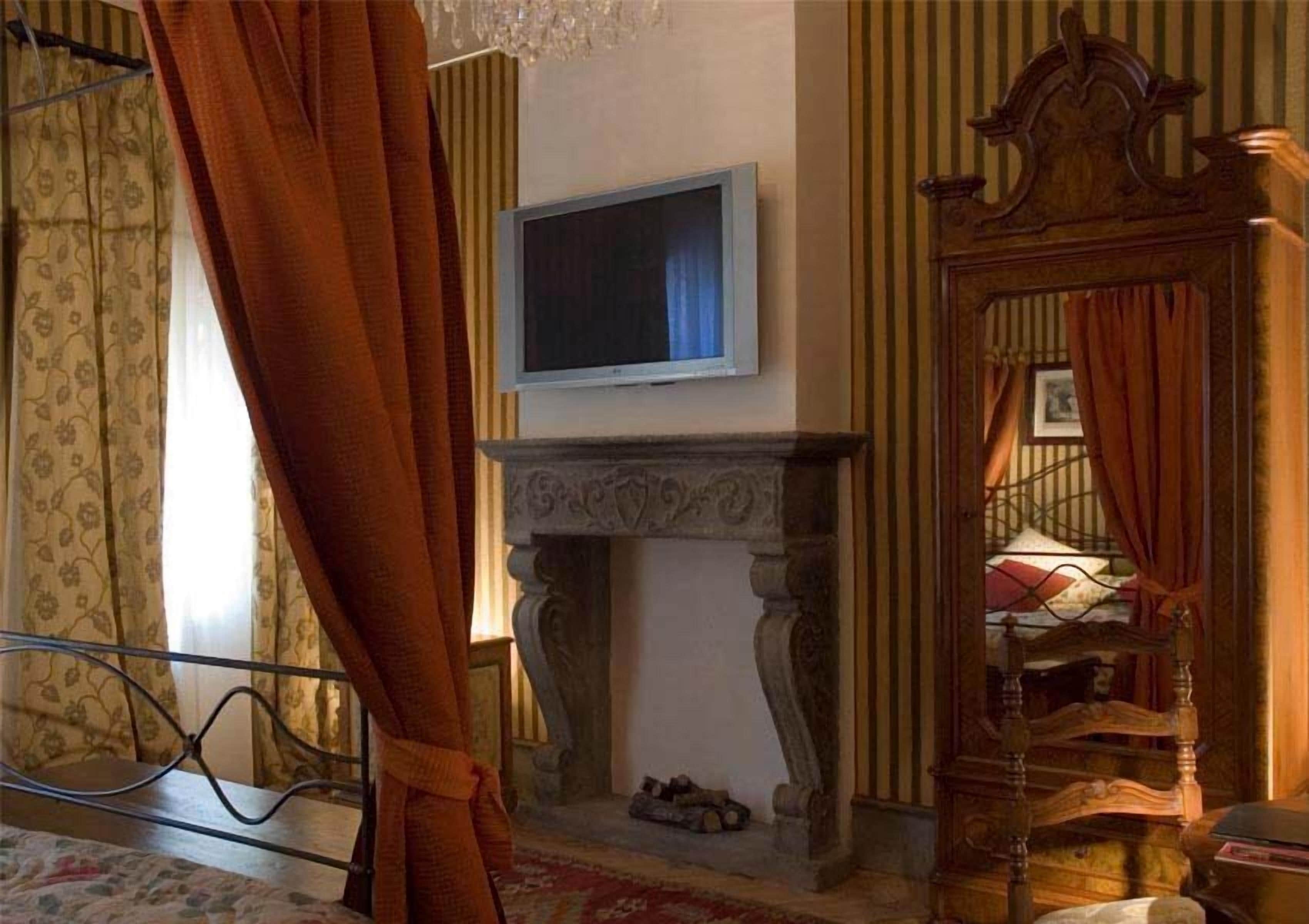 Een kamer met een televisie boven een open haard, een bed met metalen frame en een houten stoel met spiegel.
