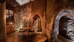 A stone-walled room with a table and chairs, a candle holder, and a window. - The Inn at the Roman Forum Luxury Collection - The Inn At The Roman Forum (Rome)