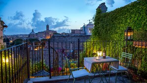 A terrace with a table and chairs, a view of a cityscape, and a wall covered in greenery. - The Inn at the Roman Forum Luxury Collection - The Inn At The Roman Forum (Rome)