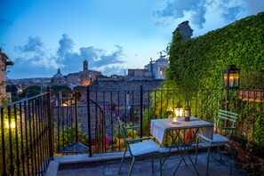 A terrace with a table and chairs, a view of a cityscape, and a wall covered in greenery. - The Inn at the Roman Forum Luxury Collection - The Inn At The Roman Forum (Rome)