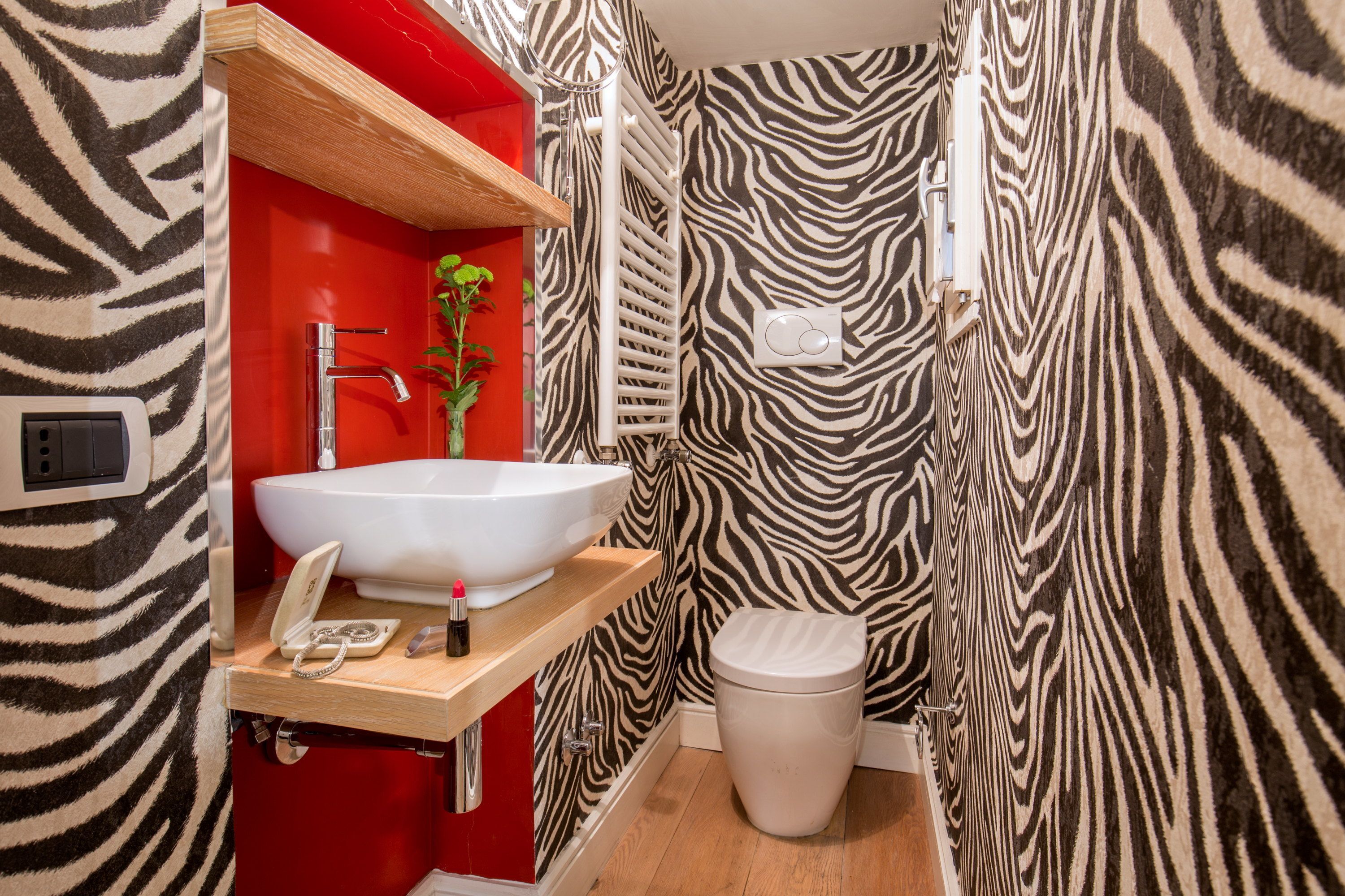 Une salle de bain avec un mur à rayures zébrées, un lavabo blanc, un meuble rouge et des toilettes.