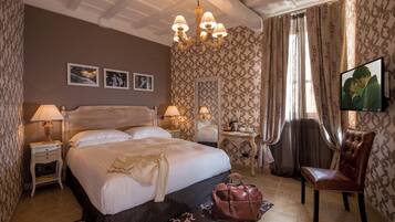 Une chambre d’hôtel avec un grand lit, deux tables de chevet, un lustre, une télévision et un papier peint à motifs.