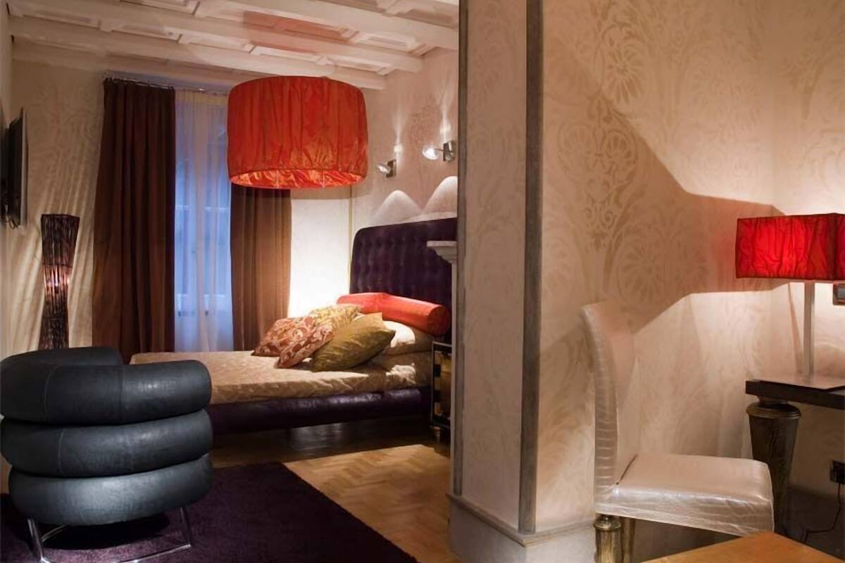 Une chambre d’hôtel avec un lit, une lampe suspendue rouge, une chaise moderne et une petite table.