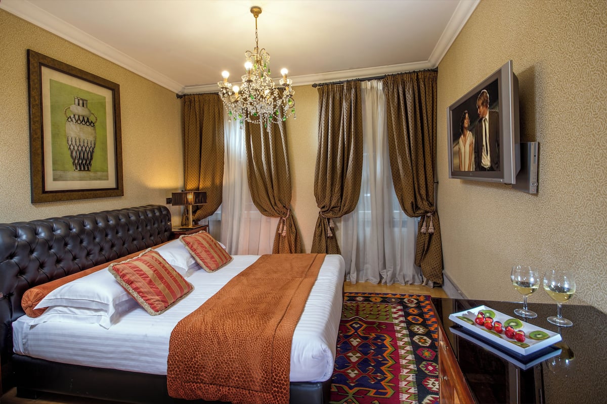 Une chambre d’hôtel avec un grand lit, un lustre, une télévision et une table avec des verres de vin.