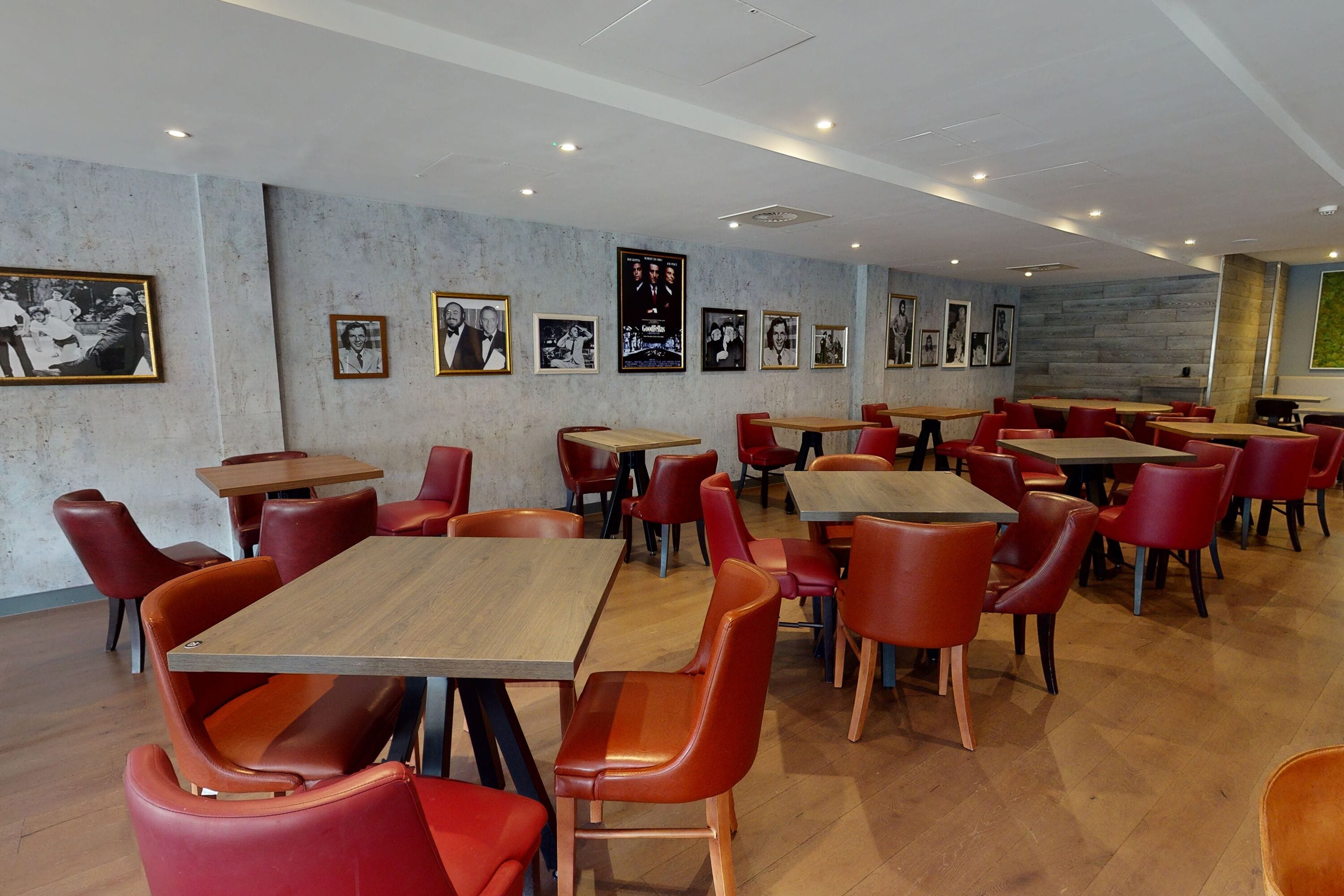 A restaurant with red chairs and wooden tables, framed pictures on the walls, and a stone accent wall.