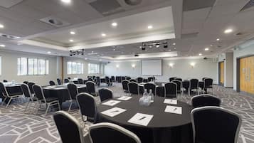 A conference room with round tables, black chairs, and a projector screen.