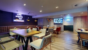 A modern restaurant with booths and tables, neon signs, and a TV screen. - Village Hotel Bournemouth (Bournemouth)