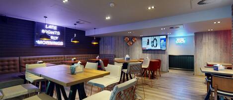 A modern restaurant with booths and tables, neon signs, and a TV screen.