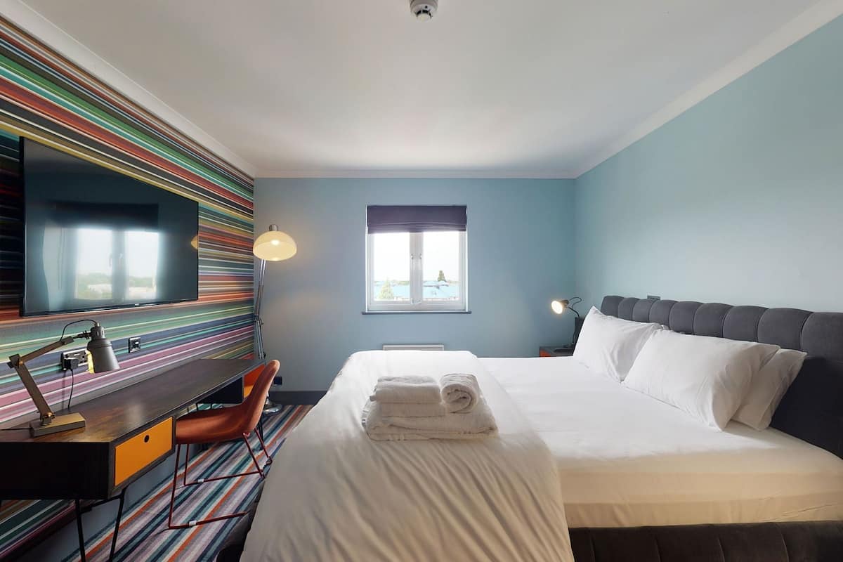 Ein Hotelzimmer mit Bett, Schreibtisch, Stuhl, Fernseher und Fenster.