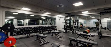 A gym with weightlifting equipment, benches, and dumbbells.