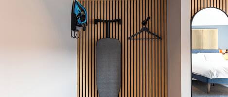 A hotel room with a wooden slat wall, a bed, a mirror, and a hanging rack with a blue bag and a hanger.