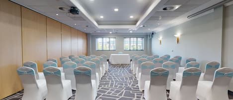 A conference room with rows of white chairs with blue sashes, a patterned carpet, and a white table at the front.