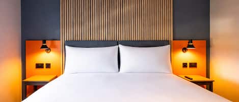 Una habitación de hotel moderna con una cama grande, dos mesitas de noche y un cabecero de madera.
