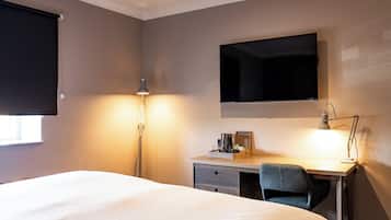 Hotellihuone, jossa on sänky, työpöytä, tuoli, lamppu ja seinälle asennettu taulutelevisio.