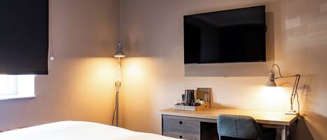 A hotel room with a bed, desk, chair, lamp, and a flat-screen TV mounted on the wall.