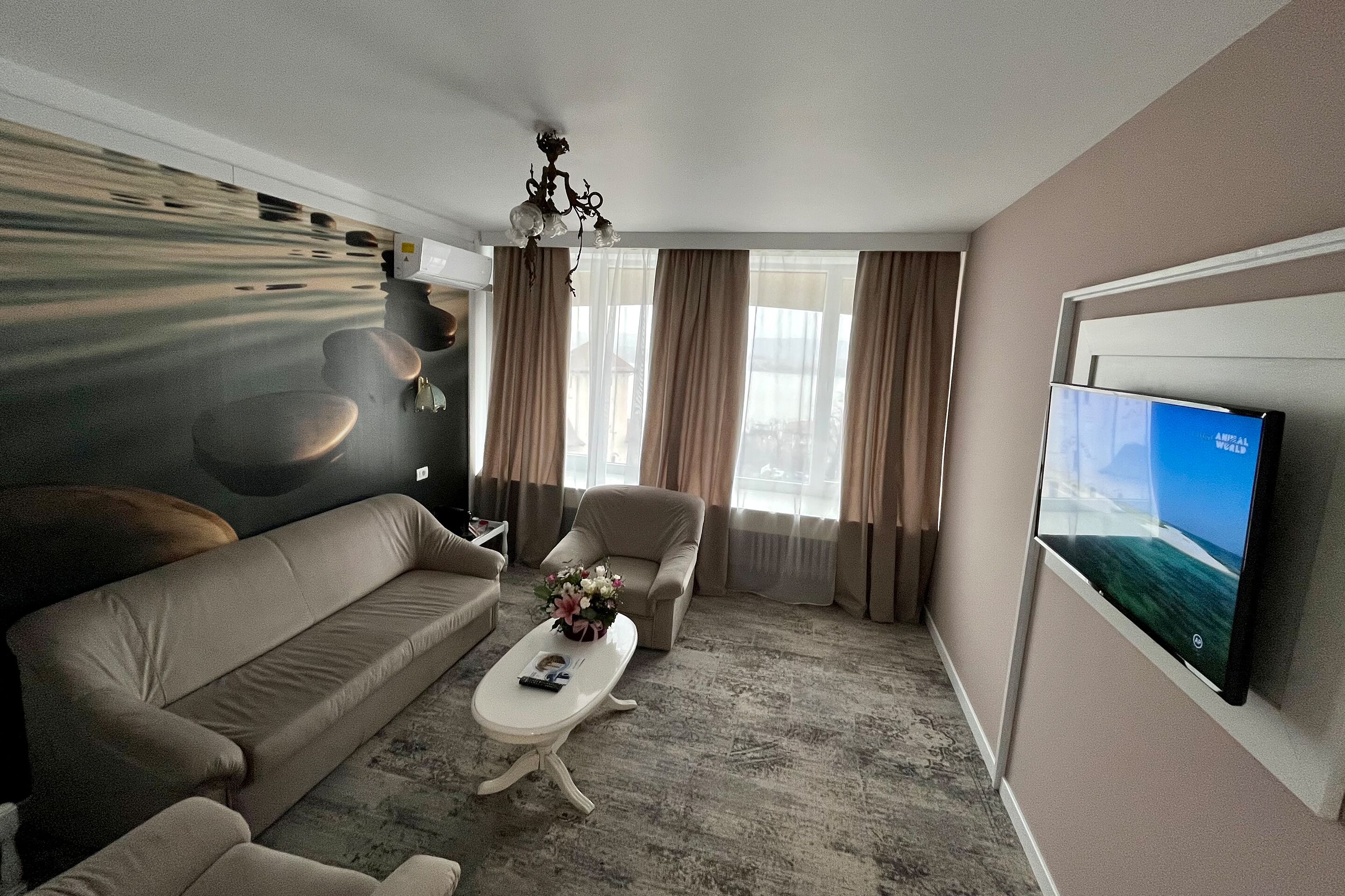 Un salon moderne avec un canapé, un fauteuil et une table basse, un lustre et un téléviseur fixé au mur.