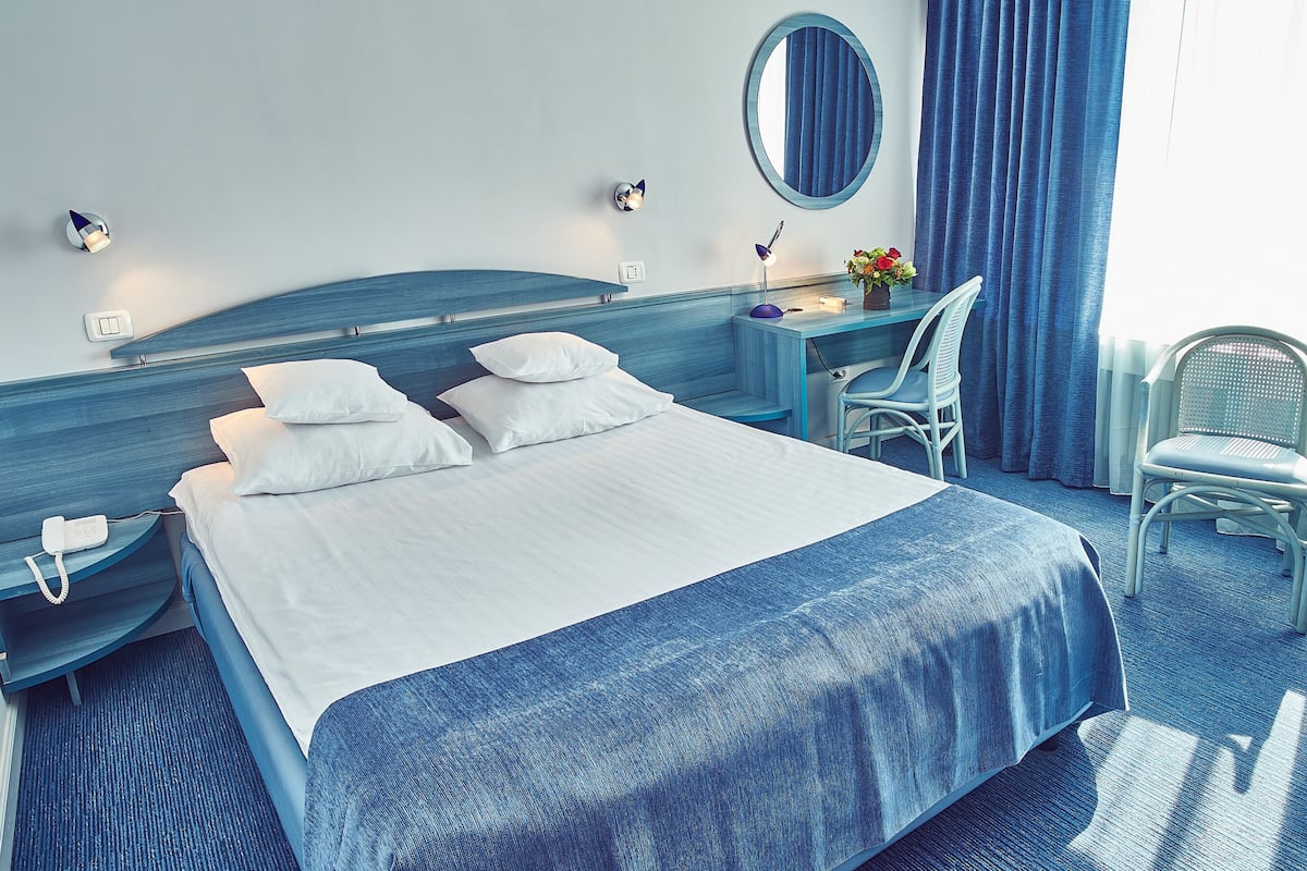 Une chambre d’hôtel avec un grand lit, un bureau, une chaise, un miroir et un téléphone.