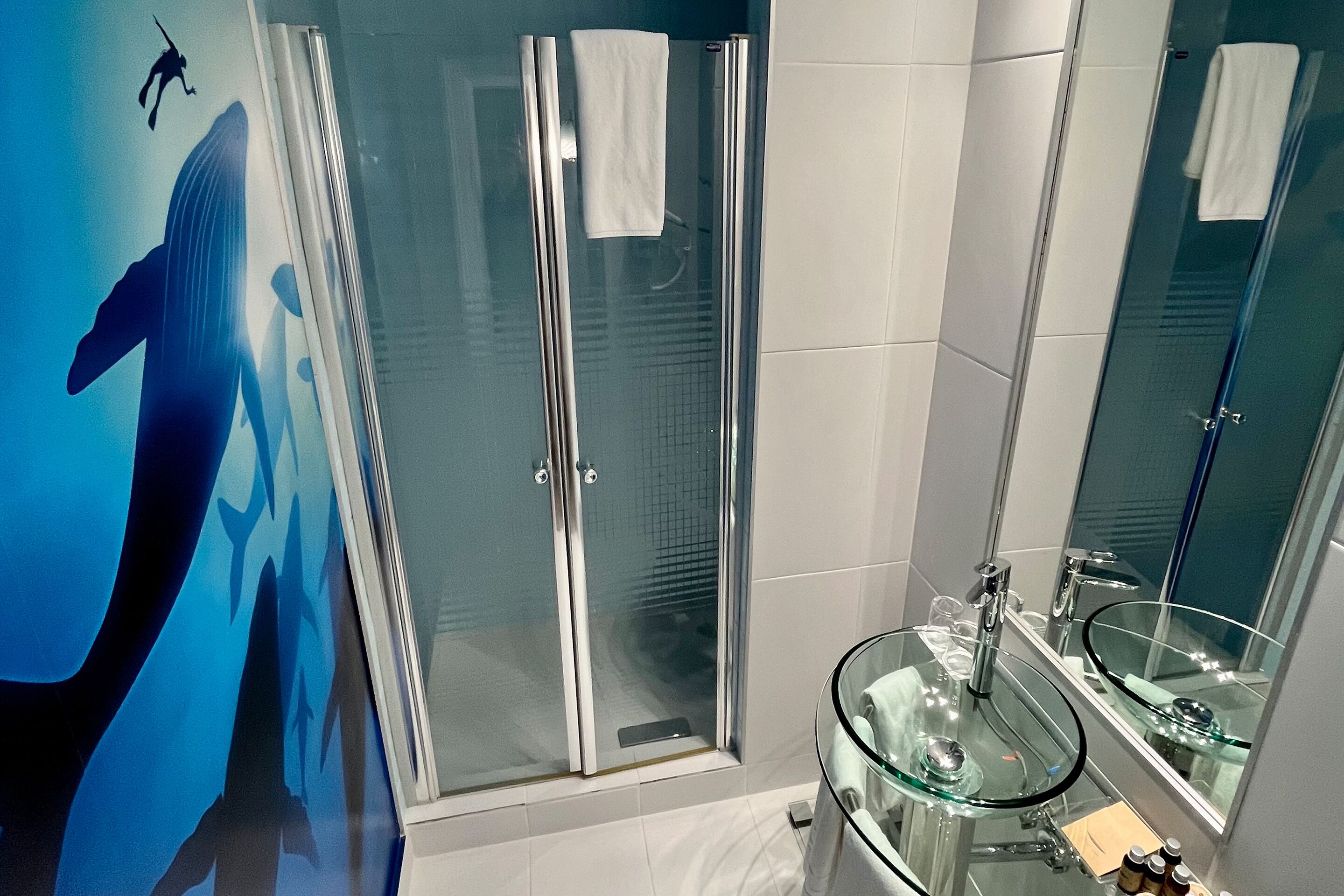 Un baño moderno con cabina de ducha de vidrio, lavabo de vidrio y un espejo grande.