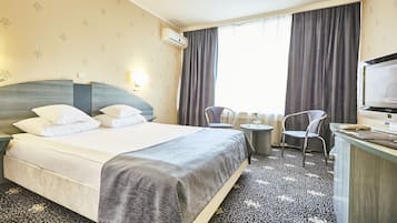 A hotel room with a bed, a desk, a chair, and a television.