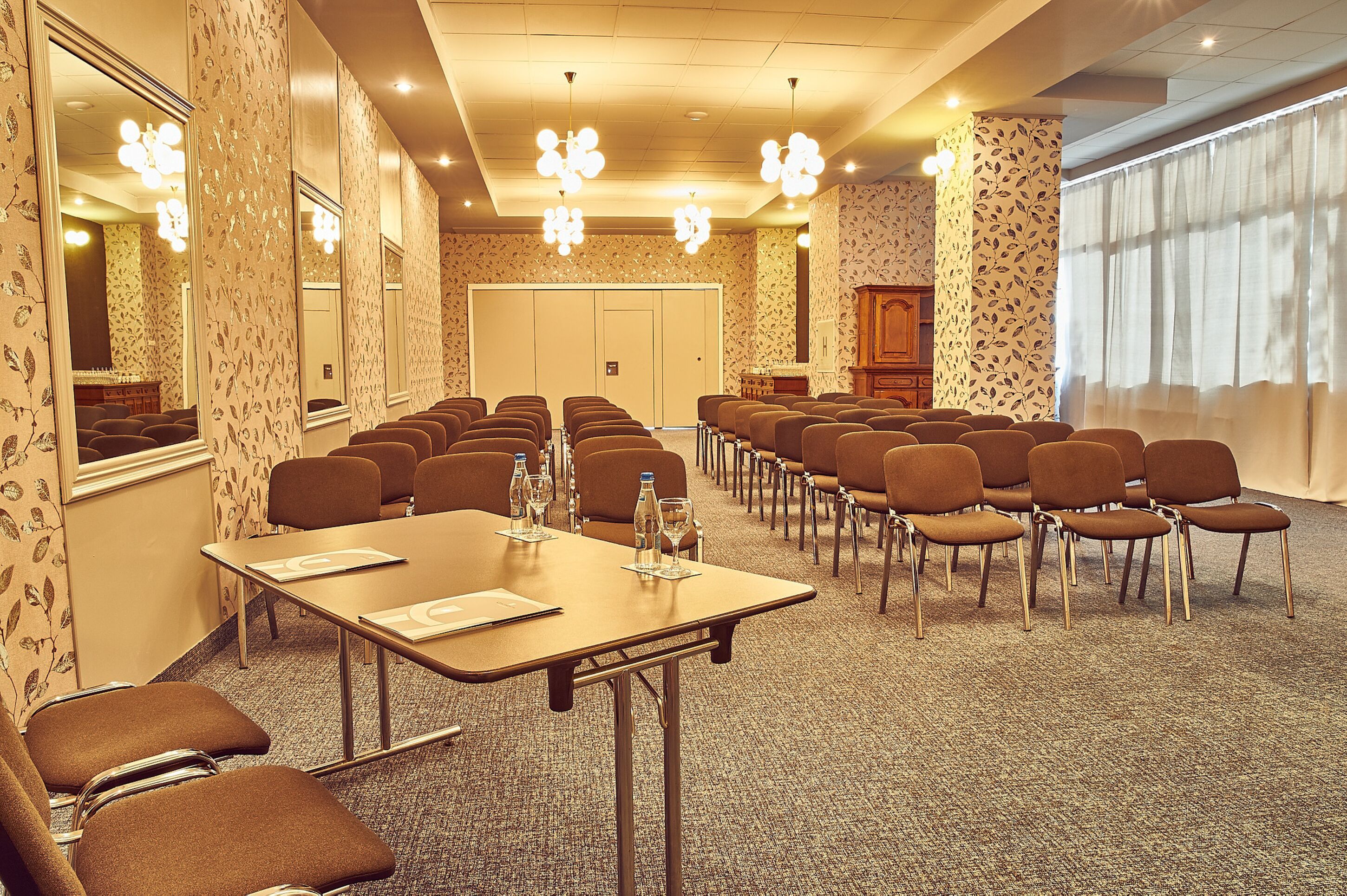 Une salle de conférence avec des rangées de chaises, des tables et un grand miroir sur l’un des murs.