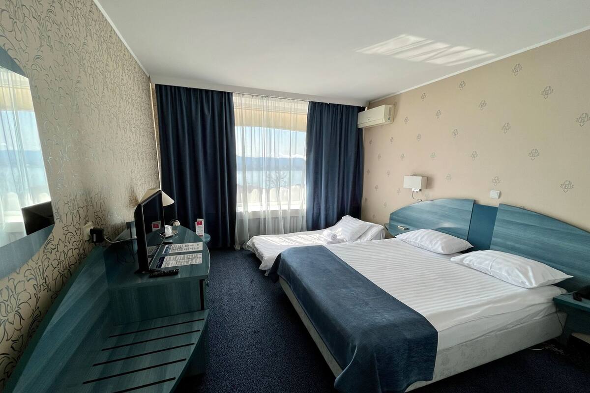 Une chambre d’hôtel avec deux lits, un bureau avec un ordinateur, une lampe et une fenêtre avec des rideaux.