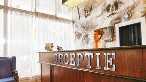 Een receptiebalie met een 'RECEPTION' bord, een groot raam met dunne gordijnen en een klok aan de muur.