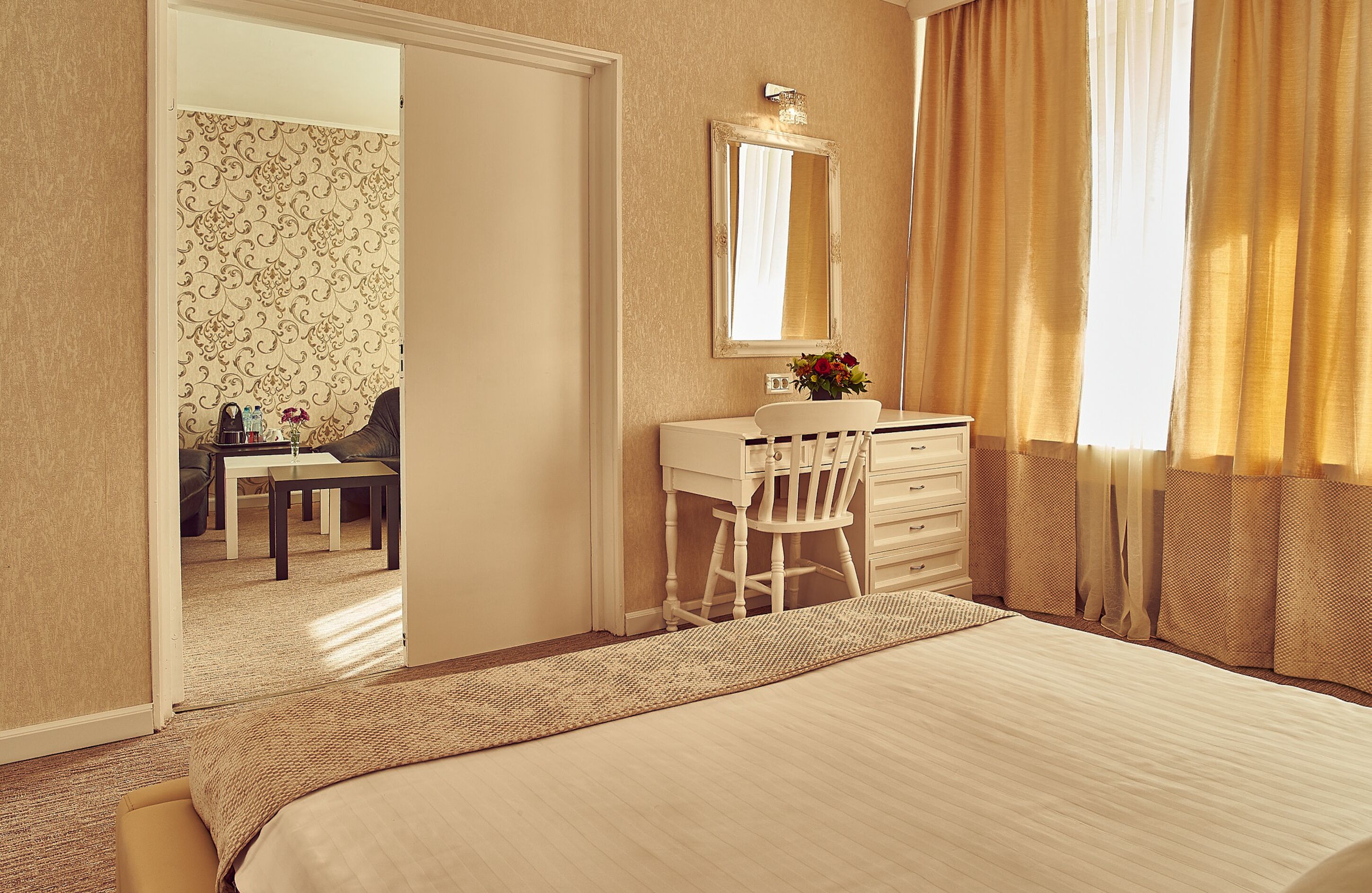 A hotel room with a bed, a desk with a chair, a dresser, a mirror, and a window with curtains.