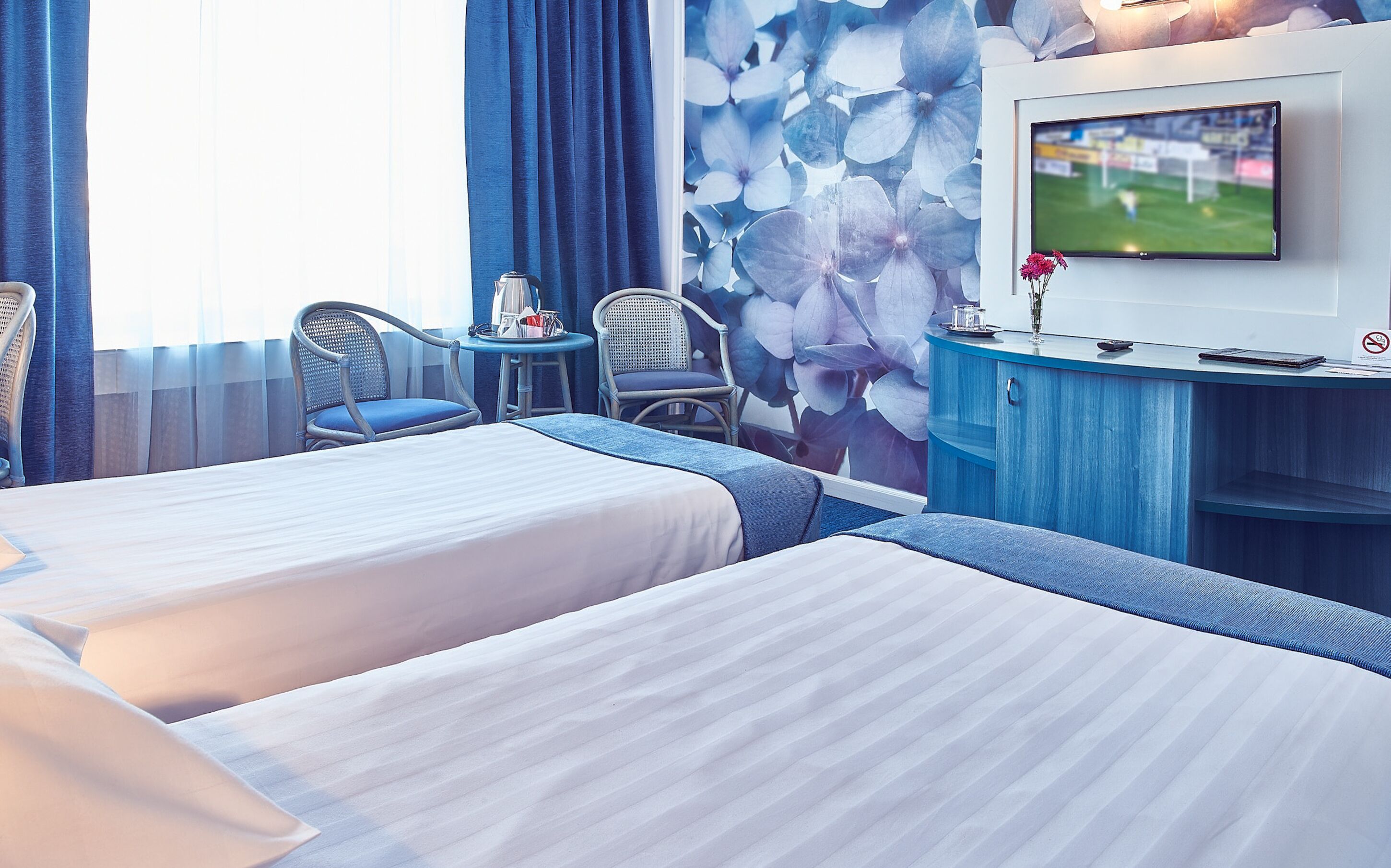 Ein Hotelzimmer mit zwei Betten, einem Fernseher, einem Schreibtisch und Stühlen.