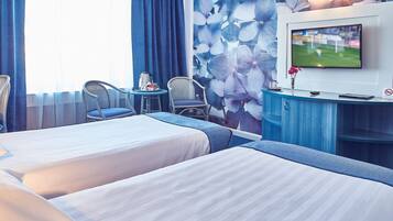 Ein Hotelzimmer mit zwei Betten, einem Fernseher, einem Schreibtisch und Stühlen.