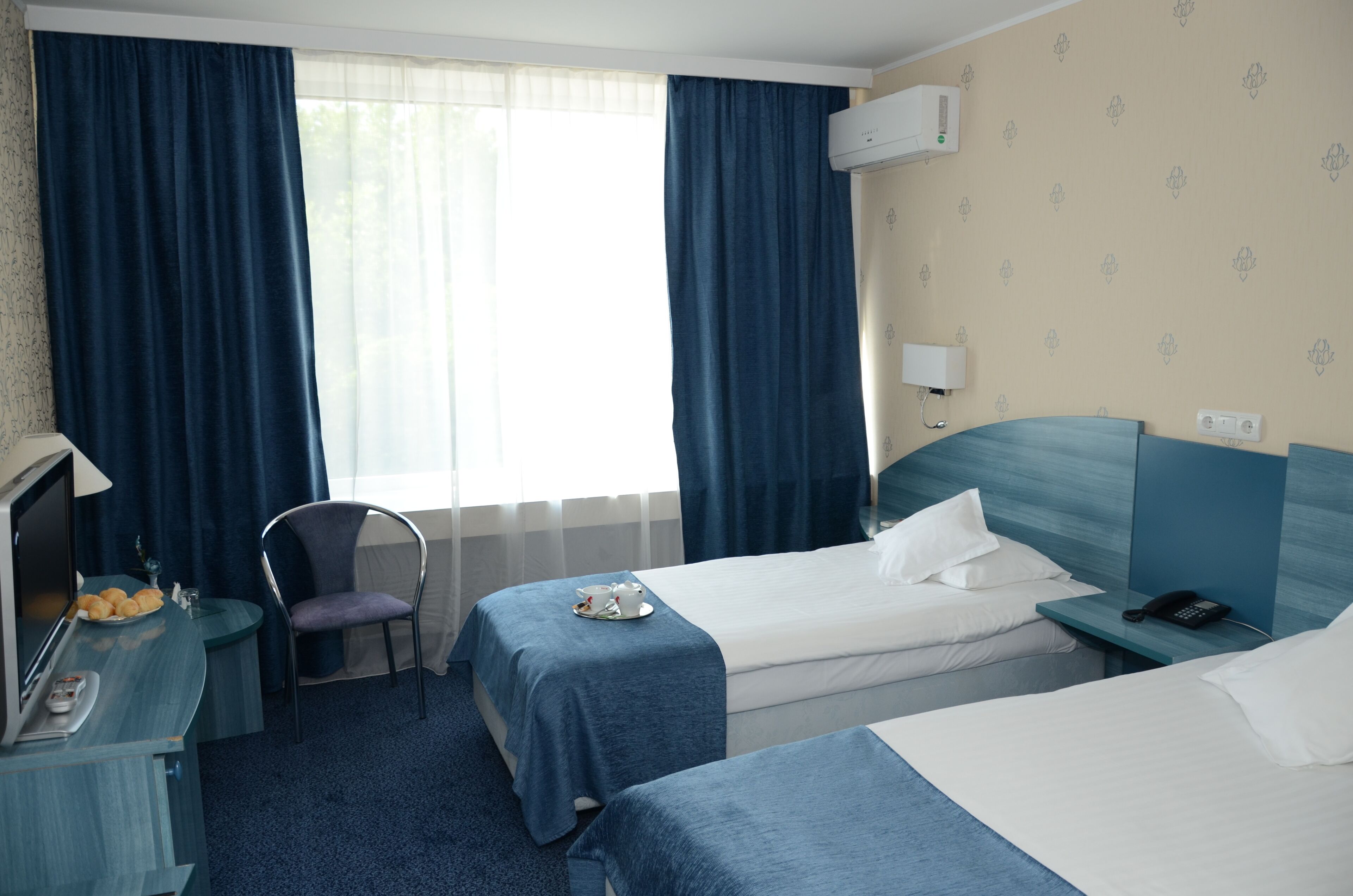 Une chambre d’hôtel avec deux lits, un bureau avec une télévision, une chaise et une fenêtre avec des rideaux.