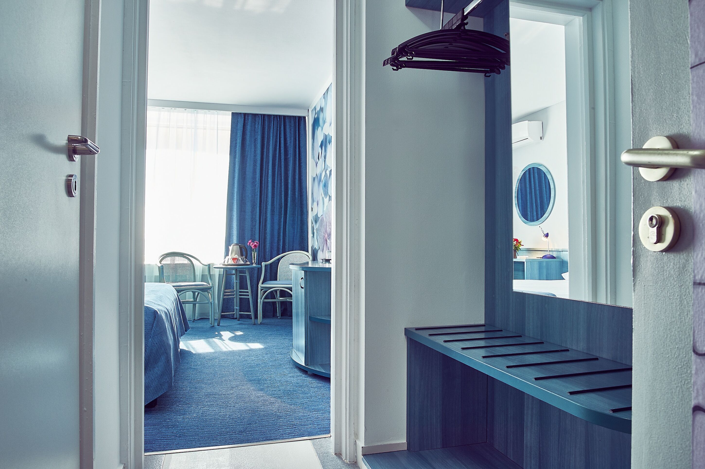 A hotel room with a bed, a desk, chairs, and a bathroom with a mirror.