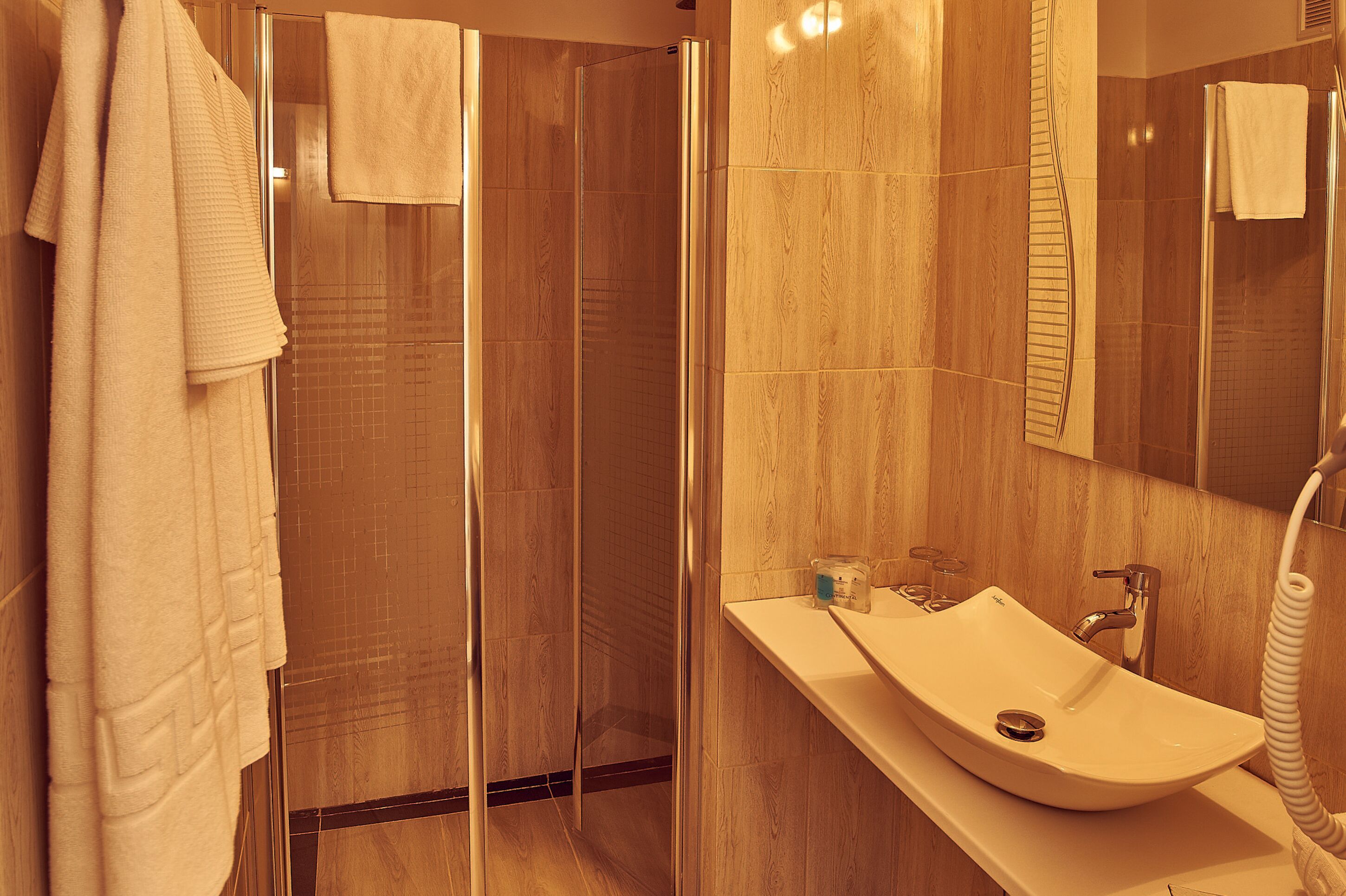 Une salle de bain moderne avec une douche à parois de verre, un grand miroir et un lavabo doté d’un porte-serviettes.
