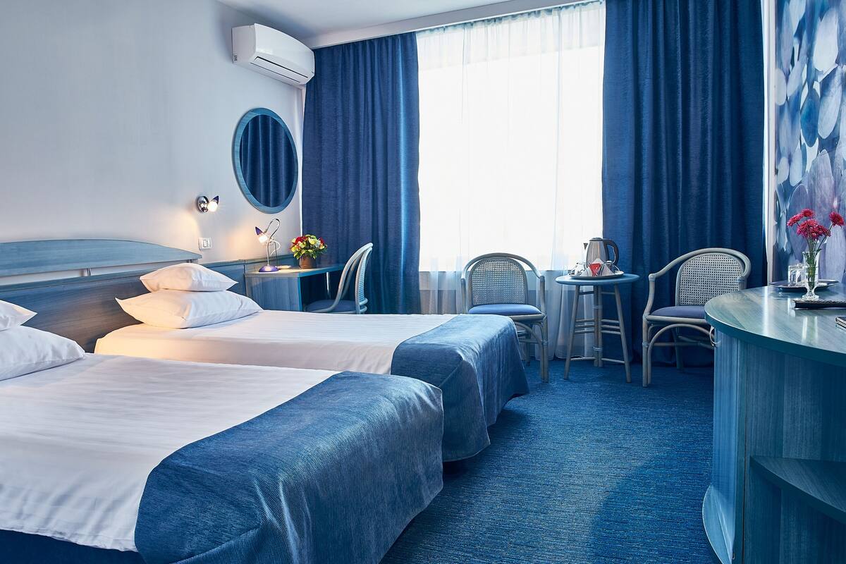Une chambre d’hôtel avec deux lits, un bureau, des chaises, une machine à café et une grande fenêtre avec des rideaux.