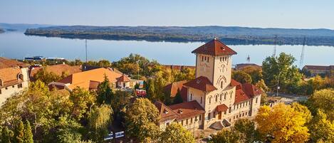 A historic building with a prominent tower, surrounded by trees and a calm lake in the background.