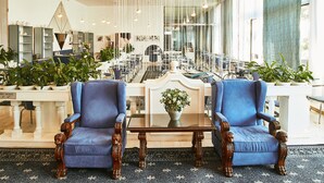 Een ruime lobby met twee blauwe fauteuils, een centrale tafel met een vaas, en een grote spiegel aan de muur.