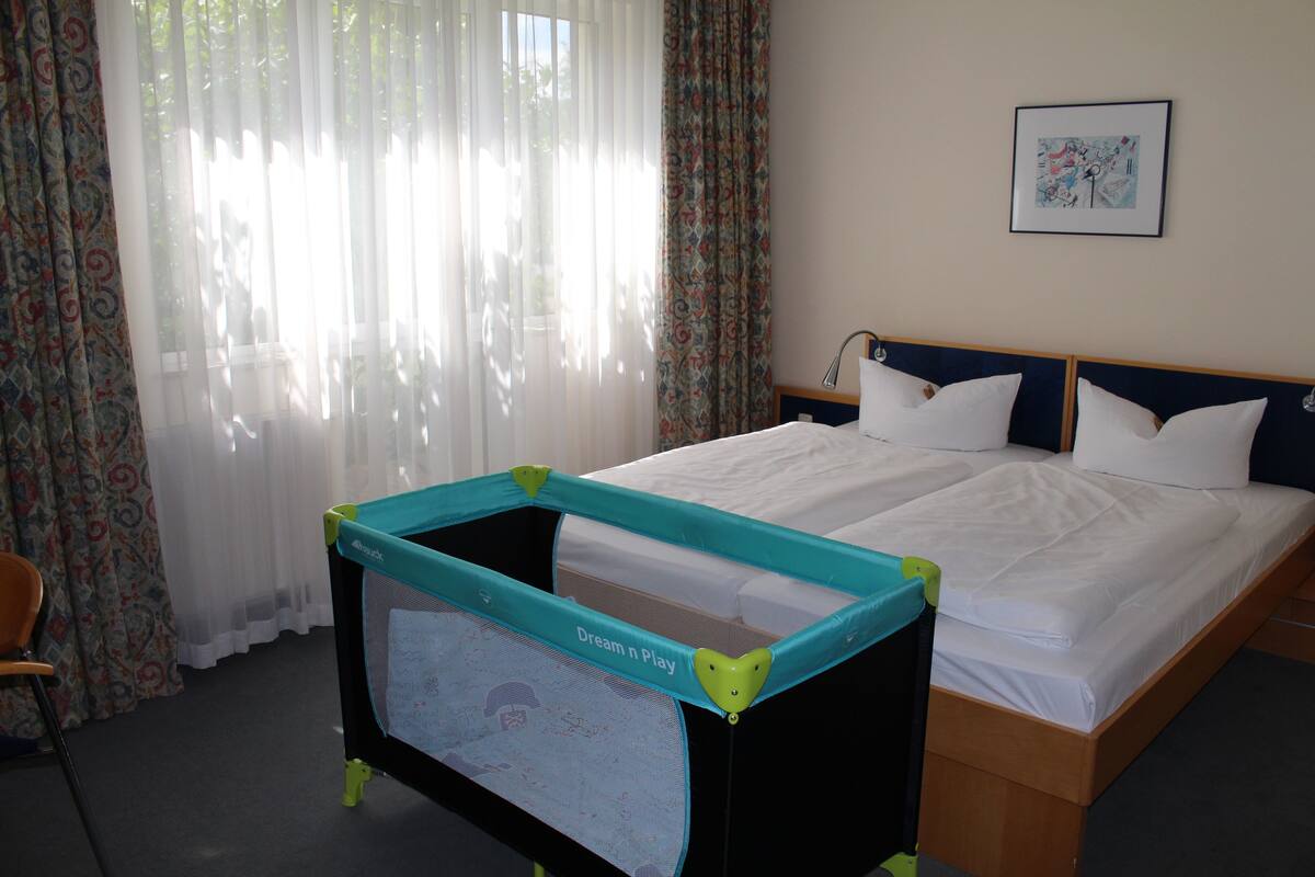 A hotel room with a bed, a crib, and a chair.