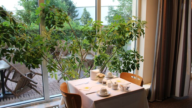 Un coin repas avec une table dressée pour deux personnes, un radiateur et une vue sur la verdure à l’extérieur.