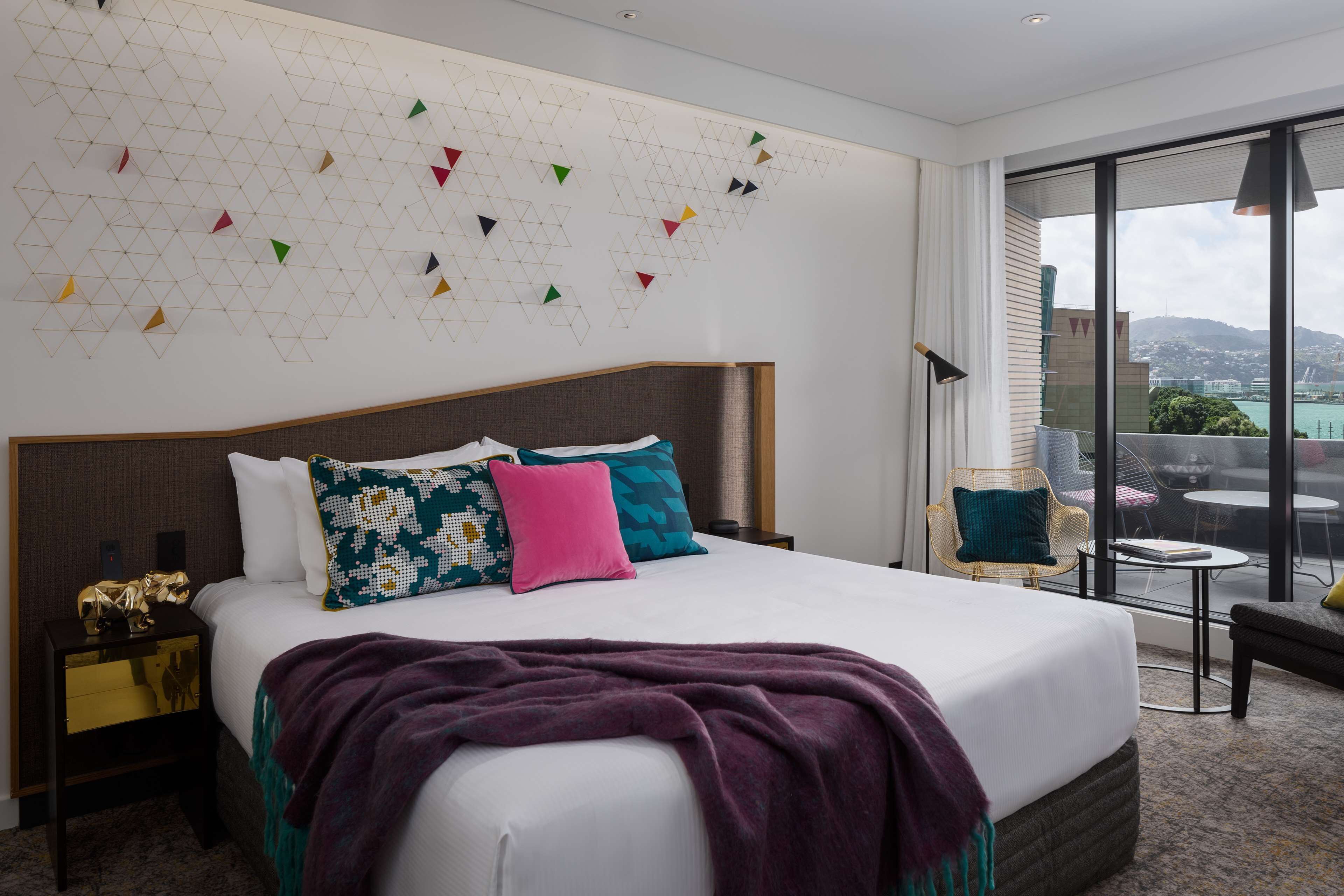 A modern hotel room with a large bed, a view of the city, and a geometric wall decoration.