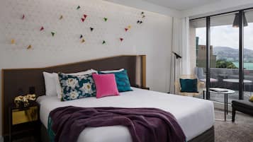 A modern hotel room with a large bed, a view of the city, and a geometric wall decoration.