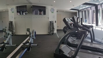Un gimnasio con equipo cardiovascular, máquinas de pesas y un espejo grande.