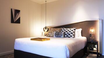 Una habitación de hotel moderna con una cama grande, una mesita de noche con lámpara y una obra de arte colgada en la pared.